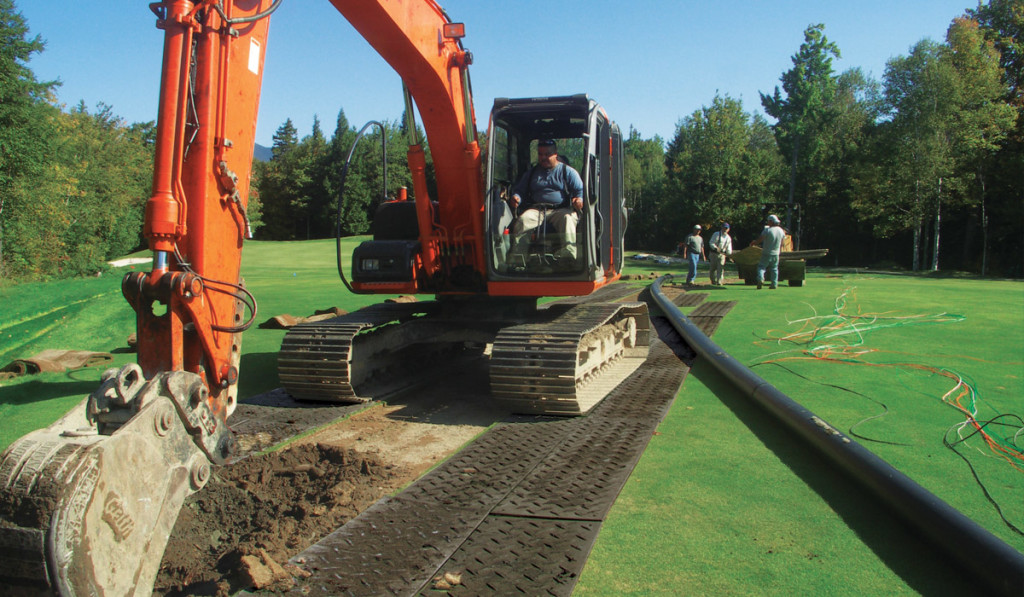 digger driving on grass protected by ground guards at a golf course