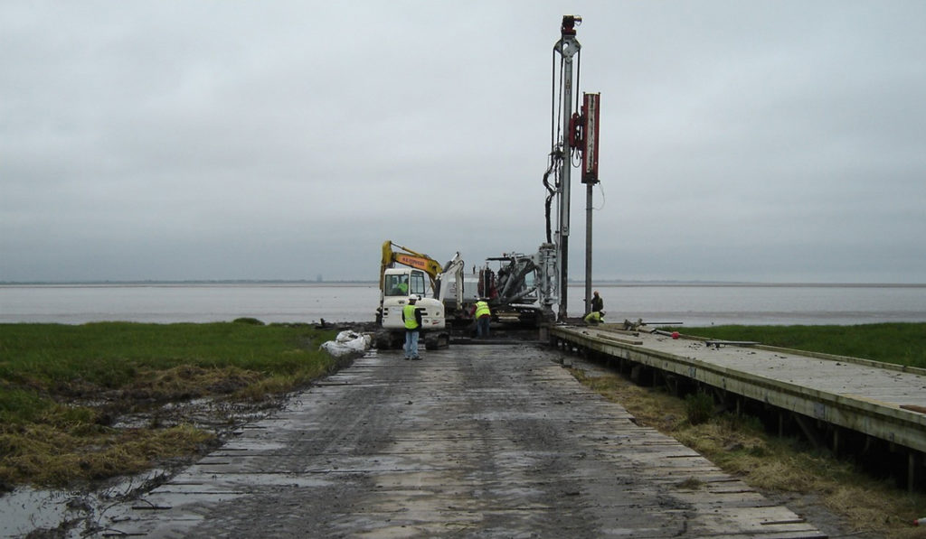 piling machine resting on bog mats on unstable ground near ocean