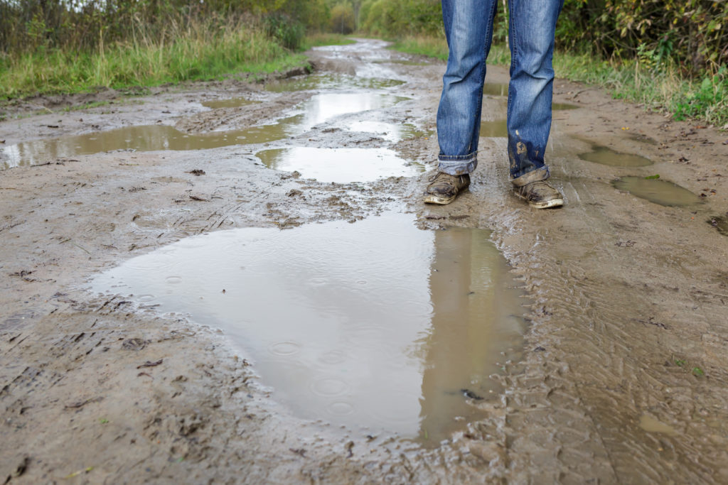 broken, wet, unstable road with scattered puddles and an individual with muddy shoes