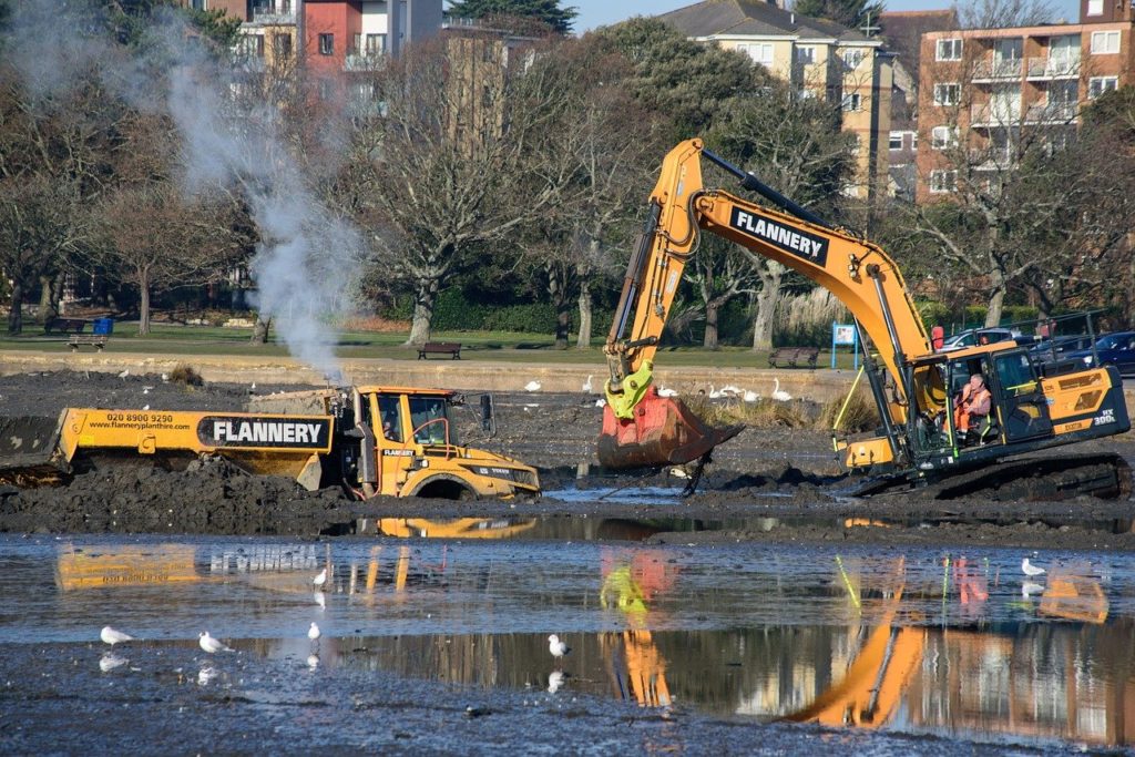 Flooded area with construction vehicle stuck in mud and excavator trying to rescue